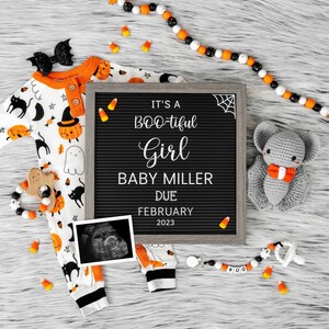 Puede incluir: Un tablero de letras negro con el texto "It's a BOO-tiful Girl Baby Miller Due February 2023". Un mameluco blanco y naranja con un estampado de Halloween en blanco y negro, un murci&eacute;lago de crochet gris y una guirnalda de ma&iacute;z dulce blanco y naranja est&aacute;n dispuestos alrededor del tablero de letras.