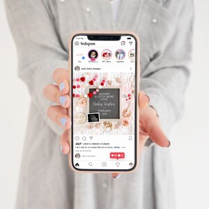 May include: A phone screen displaying an Instagram post announcing a pregnancy with the text "Adding a little more love! Baby Tayler February 2023". The post features a pink and white letter board with a heart garland and other baby-themed decorations.