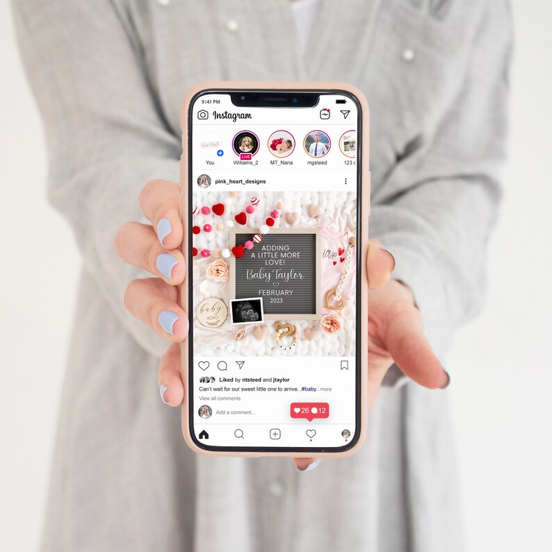 May include: A phone screen displaying an Instagram post announcing a pregnancy with the text "Adding a little more love! Baby Tayler February 2023". The post features a pink and white letter board with a heart garland and other baby-themed decorations.