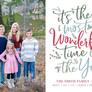 May include: A Christmas card featuring a family of five standing in a snowy forest. The card has the text "It's the most wonderful time of the year" in red, blue, and green lettering. The family's names are listed below the text: "The Smith Family | 2020".