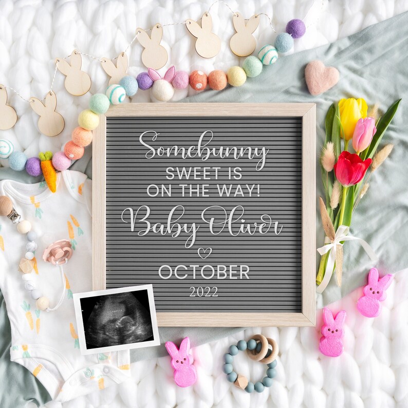 Puede incluir: Un tablero de letras gris con el texto "Somebunny sweet is on the way! Baby Oliver October 2022". El tablero est&aacute; rodeado de bolas de fieltro de colores pastel, recortes de conejitos de madera y un ramo de tulipanes amarillos y rojos.