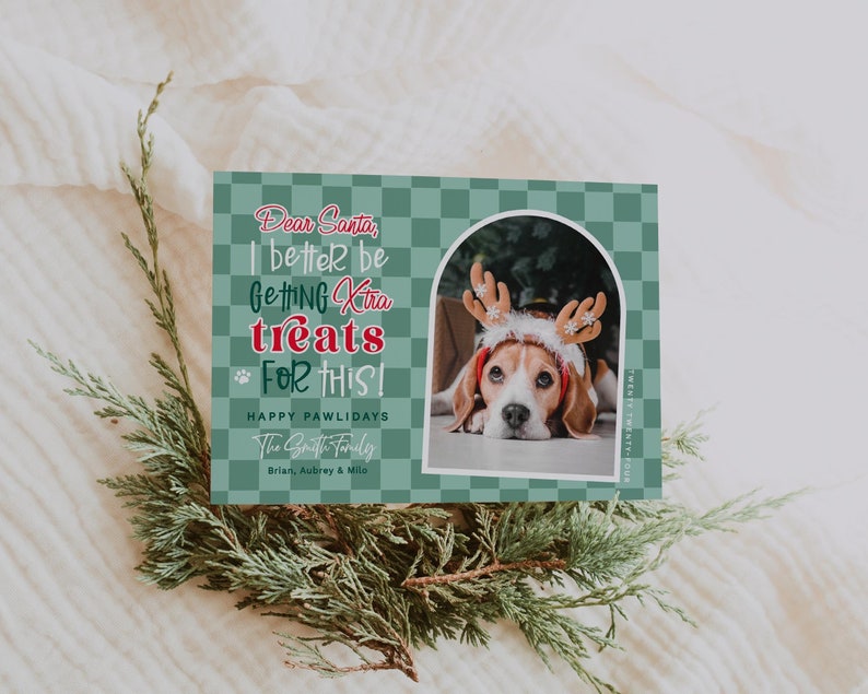 May include: A holiday greeting card with a green checkered background and the text "Dear Santa, I better be getting extra treats for this!" A photo of a beagle wearing a reindeer antler headband is featured. The card is surrounded by greenery.
