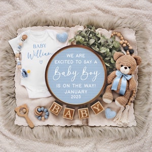 May include: A blue and white letter board with the text "We are excited to say a Baby Boy is on the way! January 2025". The board is surrounded by a white onesie with the text "Baby William", a teddy bear, wooden blocks spelling "BABY", and other baby-themed decorations.
