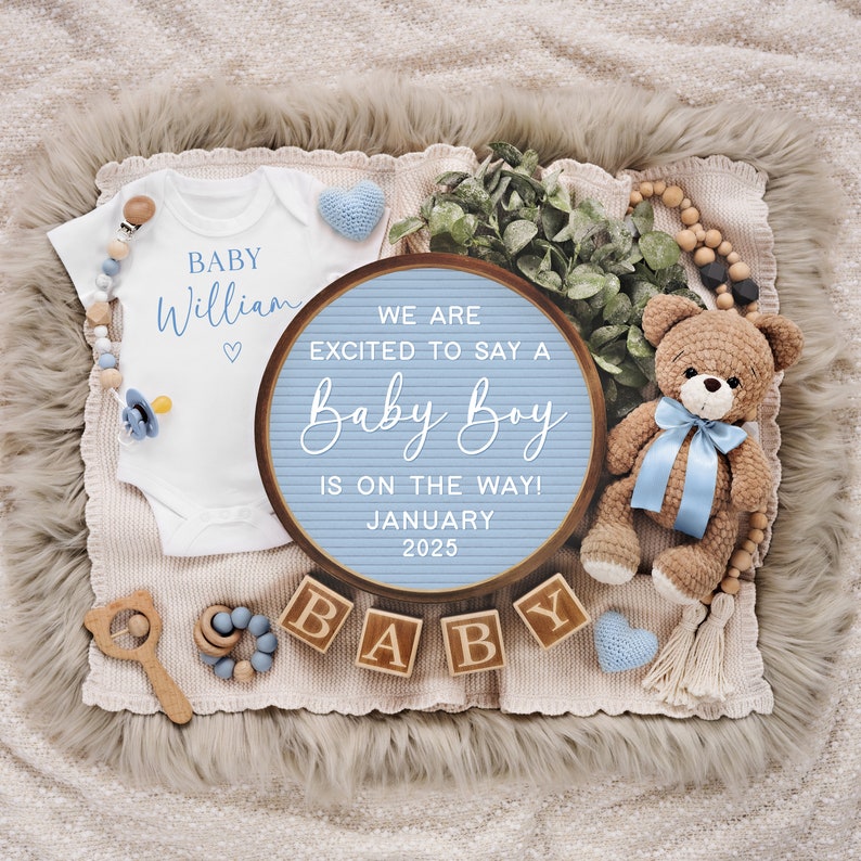 May include: A blue and white letter board with the text "We are excited to say a Baby Boy is on the way! January 2025". The board is surrounded by a white onesie with the text "Baby William", a teddy bear, wooden blocks spelling "BABY", and other baby-themed decorations.