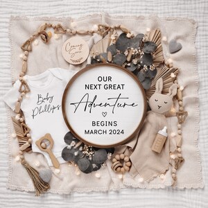 May include: A white onesie with the text "Baby Phillips" on it, a wooden sign with the text "Our next great adventure begins March 2024", a wooden sign with the text "Coming Soon", and other baby-related items on a beige background.
