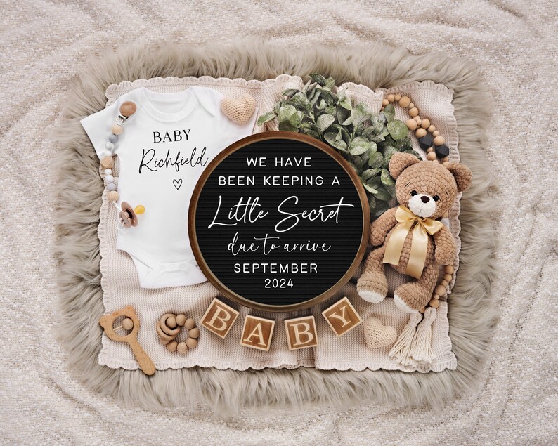 May include: A baby announcement featuring a white onesie with "BABY Richfield" printed on it, a black circular sign with text, wooden blocks spelling "BABY", and a crocheted teddy bear with a gold ribbon. The announcement is set on a neutral-toned blanket.