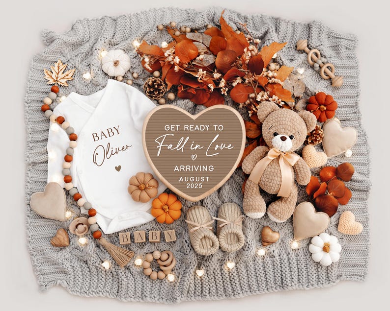 Puede incluir: Un letrero de madera en forma de coraz&oacute;n con el texto "Get ready to Fall in Love" y "Arriving August 2025". El letrero est&aacute; rodeado de decoraciones de oto&ntilde;o, incluyendo un body de beb&eacute; con el texto "Baby Oliver", un osito de peluche y un par de botines.
