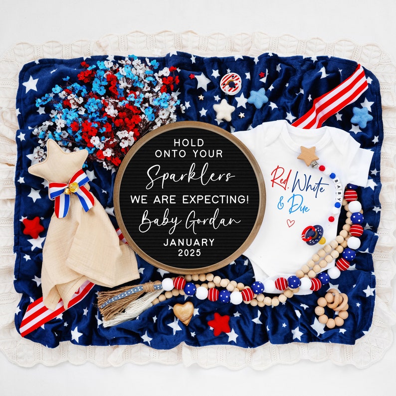 Op de afbeelding: Een letterbord met de tekst "Hold onto your sparklers. We are expecting! Baby Gordan. January 2025." Een wit rompertje met de tekst "Red White & Due" en een rood hart. Een rood-wit-blauwe stervormige deken.