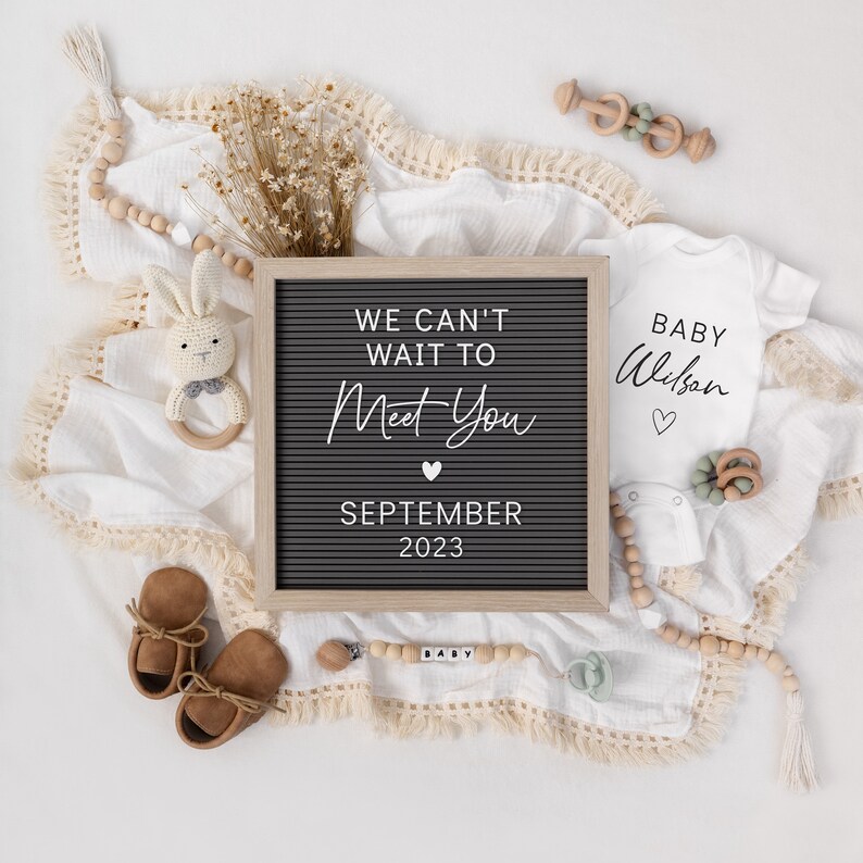 Puede incluir: Una composici&oacute;n plana de anuncio de beb&eacute;. Una pizarra gris con el texto "We can't wait to Meet You September 2023". Un body blanco con la frase "Baby Wilson". Incluye zapatos, un chupete y una sonaja de madera.
