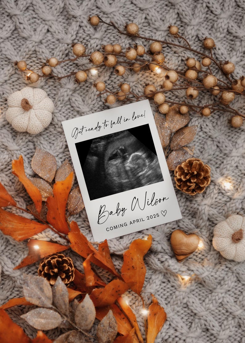 K&ouml;nnte beinhalten: Eine wei&szlig;e Karte mit einem Schwarzwei&szlig;-Ultraschallbild und dem Text "Get ready to fall in love! Baby Wilson Coming April 2025" auf einem gestrickten grauen Hintergrund mit Herbstdekorationen.
