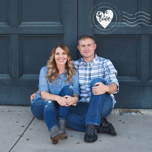 May include: A couple sits on a sidewalk in front of a dark blue door. The man is wearing a plaid shirt and blue jeans. The woman is wearing a blue shirt and blue jeans. A heart with the word "love" inside is in the upper right corner of the image. The heart is surrounded by the text "Sealed with a kiss by yours truly" and a series of wavy lines.