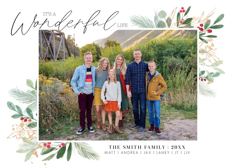 May include: A Christmas card featuring a family of six standing in front of a bridge. The card has a green and gold watercolor border with red berries. The text on the card reads "It's a Wonderful Life" and "The Smith Family 20XX".