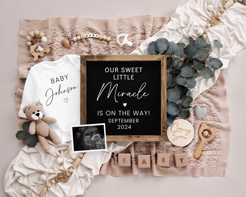 May include: A baby announcement with a white onesie that says "Baby Johnson" and a black chalkboard sign that says "Our Sweet Little Miracle is on the way! September 2024". There is also a wooden sign that says "Coming Soon" and wooden blocks that spell out "BABY".