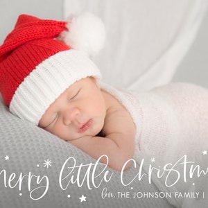 May include: A newborn baby wearing a red and white Santa hat sleeps on a gray blanket. The text "Merry little Christmas" is written in white cursive script with stars. The text "love, THE JOHNSON FAMILY | 2021" is written below in white.