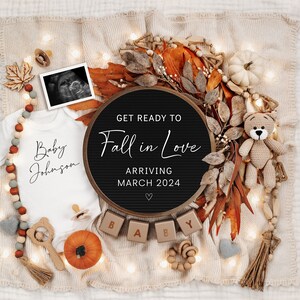 May include: A black letter board with the text "Get Ready to Fall in Love Arriving March 2024" surrounded by autumn-themed decorations, including a white onesie with the text "Baby Johnson", a small teddy bear, and a pumpkin.