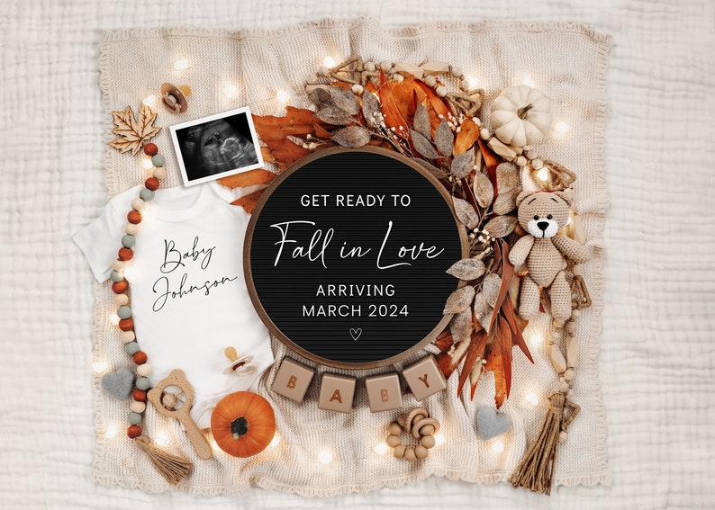 May include: A black letter board with the text "Get Ready to Fall in Love Arriving March 2024" surrounded by autumn-themed decorations, including a white onesie with the text "Baby Johnson", a small teddy bear, and a pumpkin.
