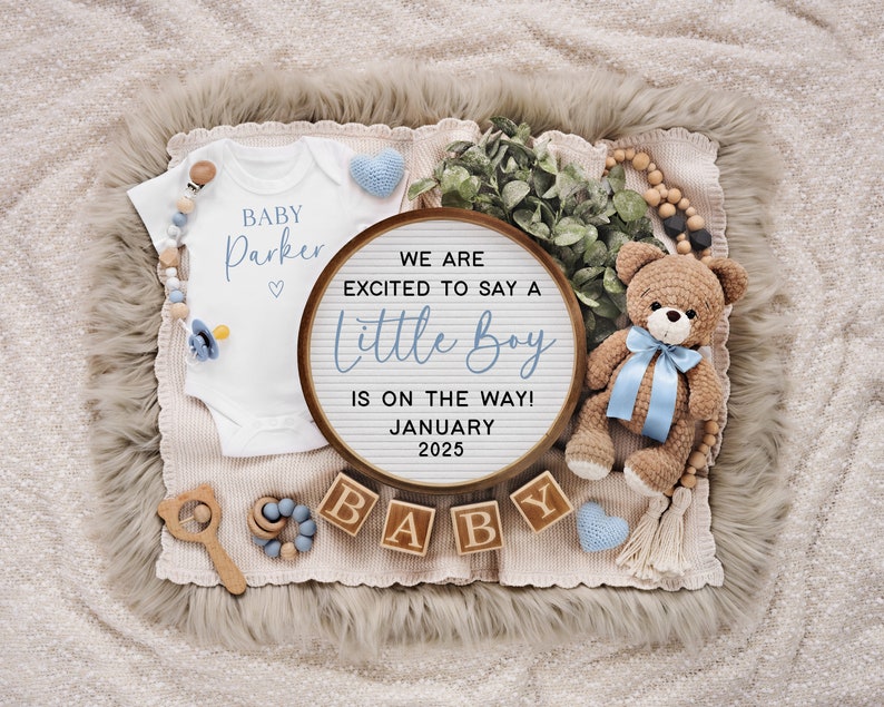 以下が含まれることがあります： 「We are excited to say a little boy is on the way! January 2025」と書かれた木製のレターボード。ボードの周りは、「Baby Parker」と書かれた白いロンパース、青いリボンをつけたテディベア、そして「Baby」と綴られた木製のブロックで囲まれています。