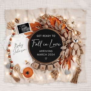 May include: A black letter board with the text "Get Ready to Fall in Love" and "Arriving March 2024" surrounded by autumn-themed decorations, including a white onesie with the text "Baby Johnson", a pumpkin, and a crocheted teddy bear.