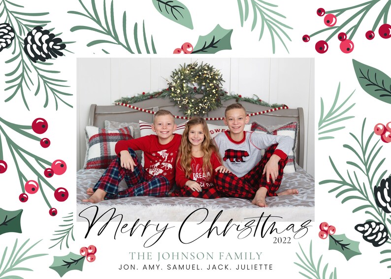 May include: A Christmas card featuring a family of five in matching pajamas. The family is sitting on a bed with a Christmas wreath behind them. The card has a green and red holly design with the text "Merry Christmas 2022" and "THE JOHNSON FAMILY JON. AMY. SAMUEL. JACK. JULIETTE".