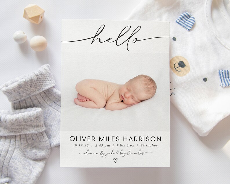 May include: A white card with black text announcing the birth of Oliver Miles Harrison. The card includes the baby's birthdate, time, weight, and length. The text "hello" is written in cursive at the top of the card. A photo of the baby sleeping is in the center of the card.