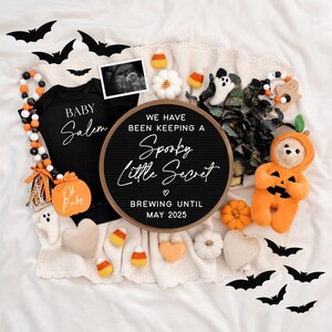 Puede incluir: Un anuncio de embarazo con tem&aacute;tica de Halloween con un tablero de letras negro que dice "We have been keeping a Spooky Little Secret Brewing Until May 2025". Hay un body negro con el texto "Baby Salem" y un oso de peluche con forma de calabaza.