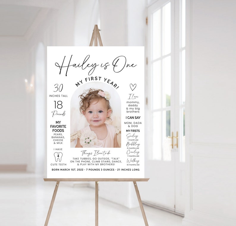 May include: A white poster with a photo of a baby girl celebrating her first birthday. The poster includes the baby's name, Hailey, and details about her first year, including her height, weight, favorite foods, and first milestones. The poster also includes a heart with the text "I love mommy, daddy & my big brothers".