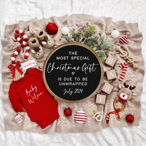 Pu&ograve; includere: Una lavagna nera con la scritta "The most special Christmas gift is due to be unwrapped July 2024". La lavagna &egrave; circondata da decorazioni natalizie rosse e bianche, un body da bambino rosso con la scritta "Baby Wilson" e blocchi di legno che compongono la parola "Baby".