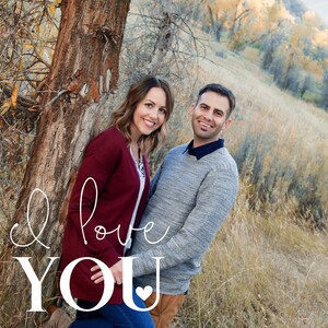 May include: A couple stands in a field with tall grass, smiling at the camera. The woman is wearing a maroon sweater and the man is wearing a gray sweater. The text "I love you" is written in white cursive script with a small heart at the end.