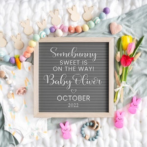 Puede incluir: Un tablero de letras con el texto "Somebunny sweet is on the way! Baby Oliver October 2022" rodeado de bolas de fieltro de colores pastel, formas de conejito de madera y un ramo de tulipanes.