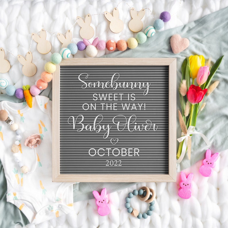 Puede incluir: Un tablero de letras con el texto "Somebunny sweet is on the way! Baby Oliver October 2022" rodeado de bolas de fieltro de colores pastel, formas de conejito de madera y un ramo de tulipanes.