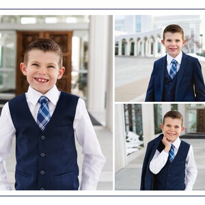 May include: A young boy wearing a navy blue suit with a white shirt and a blue and white plaid tie. He is smiling and looking at the camera. The boy is standing in front of a white building with a large door.