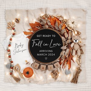 May include: A black letter board with the text "Get Ready To Fall in Love" and "Arriving March 2024" surrounded by autumnal decorations, including a white babygrow with the text "Baby Johnson", a small pumpkin, and wooden blocks spelling "BABY".