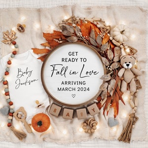 May include: A white babygrow with the text "Baby Jackson" in black script. A wooden sign with the text "Get Ready to Fall in Love Arriving March 2024" is surrounded by autumn-themed decorations, including a small teddy bear, a pumpkin, and a wreath of leaves.
