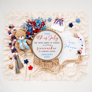 May include: A red, white, and blue themed baby announcement with a sign that reads "This 4th of July we have news to share! A little firecracker is coming soon! January 2025". There are also wooden blocks that spell out "BABY", a teddy bear, a baby onesie, and other patriotic decorations.