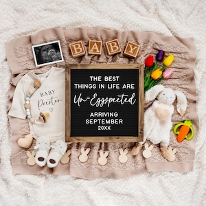 May include: A black letter board with the text "The best things in life are Un-Eggspected" and "Arriving September 20XX".  The board is surrounded by a white baby onesie with the text "Baby Preston", a white bunny rabbit toy, a pacifier, a pair of baby booties, and a string of wooden bunny rabbit cutouts.