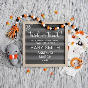 May include: A Halloween-themed baby announcement with a letter board that reads "trick or treat! Our family is growing two little feet Baby Smith arriving March 2022". There is a crocheted gray bat, a white onesie with a black cat and orange pumpkins, and a beaded necklace with orange and black beads.