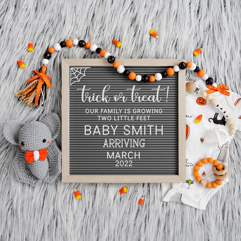 May include: A Halloween-themed baby announcement with a letter board that reads "trick or treat! Our family is growing two little feet Baby Smith arriving March 2022". There is a crocheted gray bat, a white onesie with a black cat and orange pumpkins, and a beaded necklace with orange and black beads.