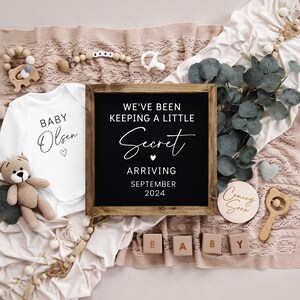 Op de afbeelding: Een baby-aankondiging met een wit rompertje met de tekst "Baby Olsen" en een zwart schoolbord met de tekst "We've been keeping a little secret arriving September 2024".