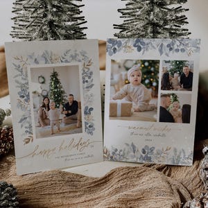 May include: Two Christmas card designs with a watercolor floral border. The first card features a family of three standing in front of a Christmas tree. The second card features a collage of photos of a baby girl. The text on the first card reads "Happy Holidays" and "The Henderson Family". The text on the second card reads "Warmest Wishes" and "Thomas & Isabella".