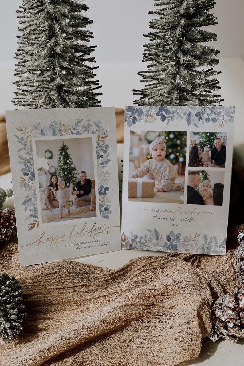 May include: Two Christmas card designs with a watercolor floral border. The first card features a family of three standing in front of a Christmas tree. The second card features a collage of photos of a baby girl. The text on the first card reads "Happy Holidays" and "The Henderson Family". The text on the second card reads "Warmest Wishes" and "Thomas & Isabella".