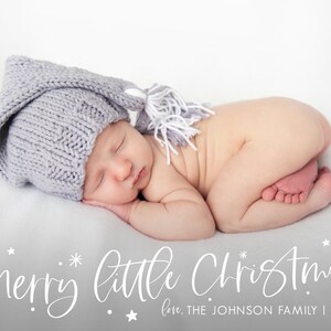 May include: A newborn baby wearing a gray knitted hat with a white tassel, sleeping on a white blanket. The text "Merry little Christmas" is written in white cursive script below the baby, with the words "love, THE JOHNSON FAMILY | 2021" written below the text.