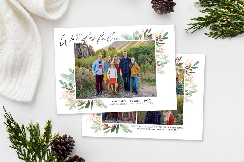 Op de afbeelding: Een kerstkaart met een aquarelrand van groene bladeren en rode bessen. De kaart toont een familiefoto van zeven mensen die voor een houten brug staan. De tekst op de kaart luidt "It's a Wonderful Life" en "The Smith Family 20XX Matt | Andrea | Jax | Laney | Liv".