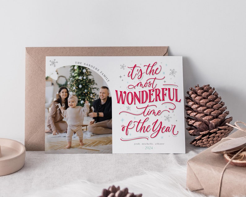 May include: A white Christmas card with a red and white 'It's the most wonderful time of the year' message. The card features a photo of a family with a Christmas tree in the background. The text 'The Sanders Family' is at the top of the card.