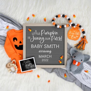 May include: A Halloween-themed baby announcement with a letter board that reads "A little Pumpkin is joining our Patch! Baby Smith arriving March 2022". There is an orange onesie with a jack-o-lantern face, a black and white ultrasound image, a wooden rattle, and a gray crocheted bat.