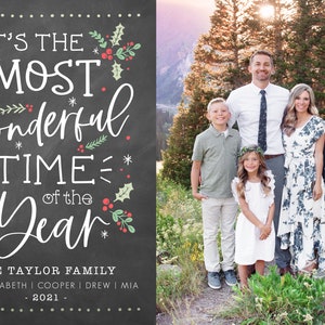 May include: A Christmas card with a chalkboard background featuring the text "It's the Most Wonderful Time of the Year." The card also includes a photo of a family of six standing in front of a mountain range. The family is dressed in casual clothing and smiling.