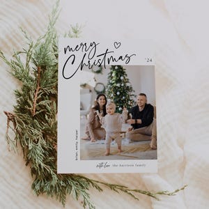 May include: A Christmas card with a photo of a family with a young child standing in front of a Christmas tree. The card reads "merry Christmas '24" with a heart symbol and "with love the Harrison family".