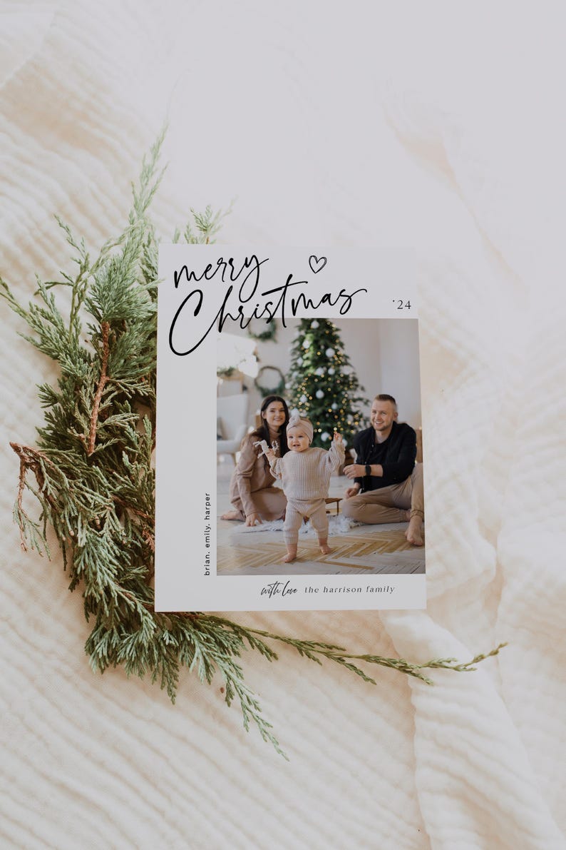 May include: A Christmas card with a photo of a family with a young child standing in front of a Christmas tree. The card reads "merry Christmas '24" with a heart symbol and "with love the Harrison family".