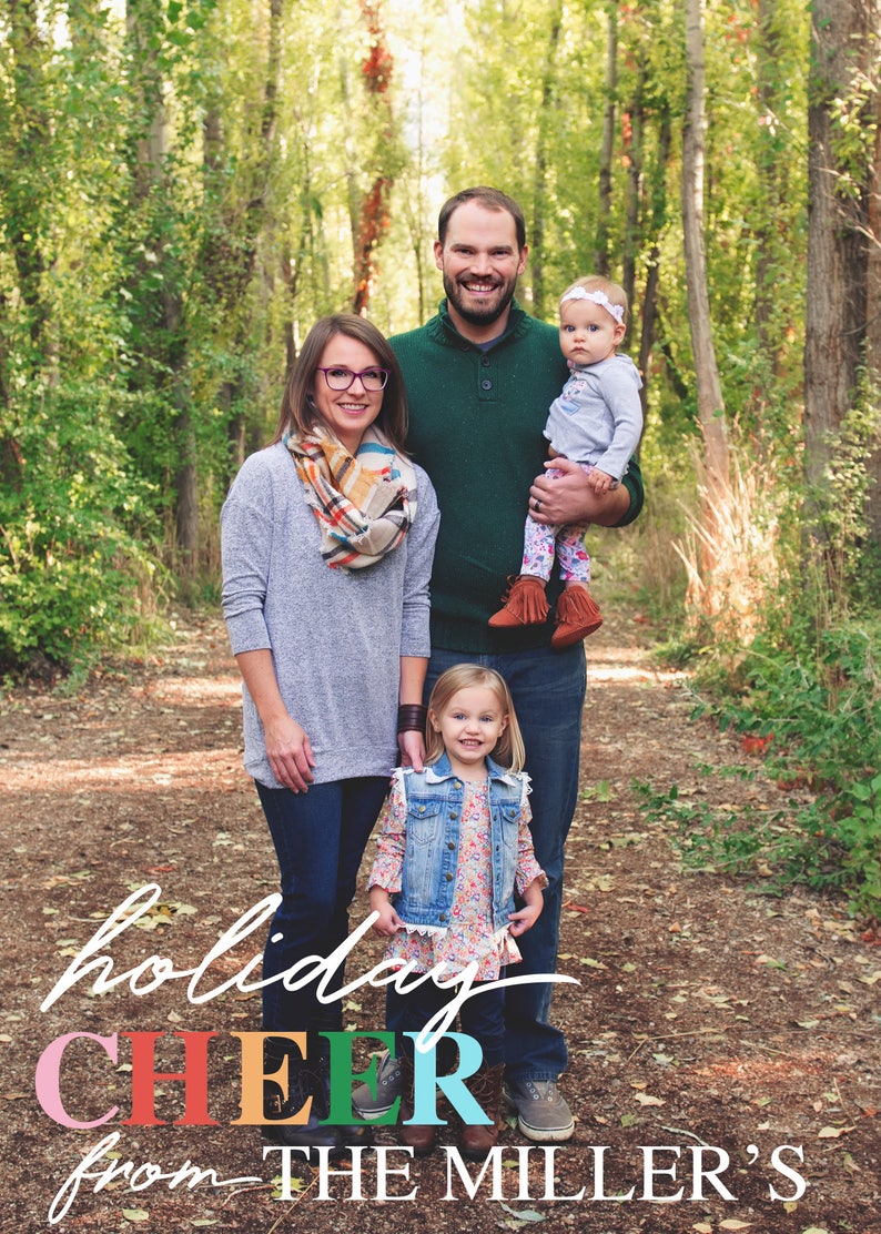 May include: A family of four standing in a wooded area. The parents are smiling and holding their two young daughters. The text "holiday CHEER from THE MILLER'S" is written in colorful letters at the bottom of the image.