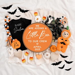 May include: A Halloween-themed baby announcement with a letter board that reads "We are adding a little boo to our crew April 2025". The letter board is surrounded by a variety of Halloween decorations, including bats, pumpkins, and a stuffed pumpkin-shaped bear.