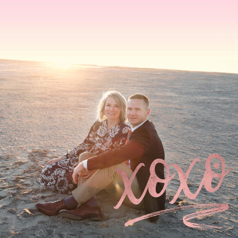 May include: A couple sits on a sandy beach at sunset, smiling at the camera. The word "xoxo" is written in pink script in the foreground.